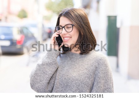 Young beautiful woman wearing glasses smiling confident talking on the phone and walking on the street at the city town