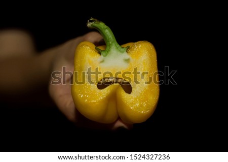 hand holds sweet yellow Bell pepper sliced in half on a black background