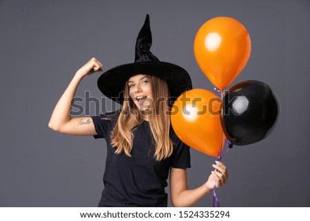 Young witch holding black and orange air balloons making strong gesture