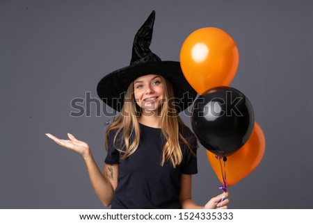 Young witch holding black and orange air balloons holding copyspace imaginary on the palm