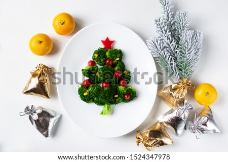 Christmas edible tree made from broccoli, tomato and corn on a white plate. Christmas card with gifts and dietary salad. Royalty-Free Stock Photo #1524347978