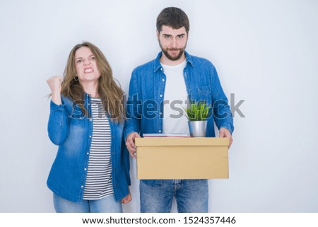 Young couple holding cardboard box moving to new house over white isolated background annoyed and frustrated shouting with anger, crazy and yelling with raised hand, anger concept