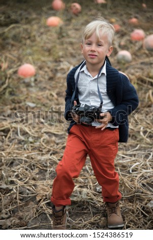 
boy in autumn clothes with a camera in his hands. pumpkin field