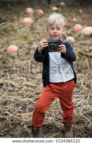 
boy in autumn clothes with a camera in his hands. pumpkin field