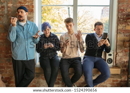 Group of happy caucasian young people standing behind the window. Sharing a news, photos or videos from smartphones, talking or playing games and having fun. Social media, modern technologies.