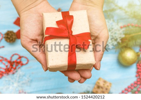 hands, palms holding gift box craft paper with red bow on the blue painted wooden background close up