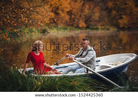 
young beautiful couple. A loving couple in the autumn park on the lake floating on a boat with oars. A girl in a red dress and a guy in a gray coat. Top view. Kiev. Ukraine. Horizontal image.