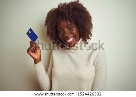 Young african afro woman holding credit card standing over isolated white background with a happy face standing and smiling with a confident smile showing teeth