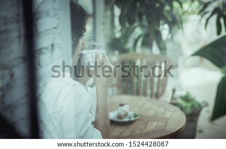 soft focus and vintage picture style asian women sitting drinking hot tea and cake in a clear glass  room at morning