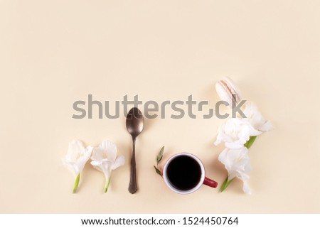 Minimalistic still life with coffee or tea, dessert and flowers on a pastel background. Cup of americano or espresso, spoon, macaroon and white gladiolus on a beige paper background. Copy space