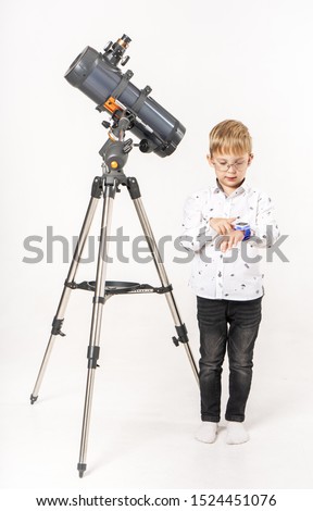 A little boy waiting for an astronomical event sits near a telescope and looks at his watch.