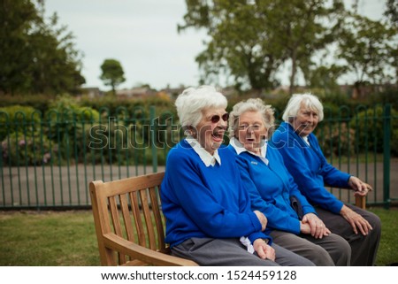 A close-up shot of senior women sitting on a bench at a bowling green laughing. 