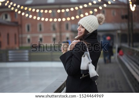 Charming young woman in the Park near the ice rink. Smiling brunette with skates, winter leisure and relaxation