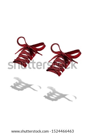 The photo of red shiny shoelaces with red tips, hanging in the air on a white background. Shoelaces is casting a shadow. 