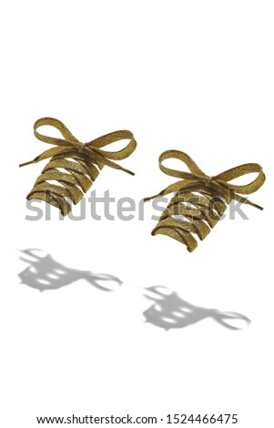 The photo of yellow shiny shoelaces with yellow tips, hanging in the air on a white background. Shoelaces is casting a shadow. 