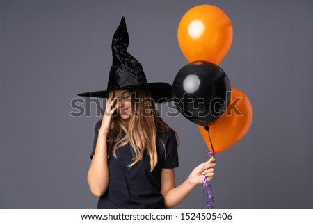 Young witch holding black and orange air balloons laughing