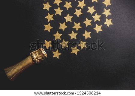 Bottle of champagne with gold confetti on black background. Top view, flat lay. Christmas celebration concept