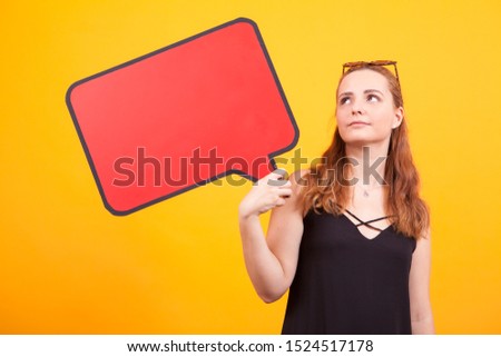 Thoughtful young woman holding an empty bubble in studio over yellow background.