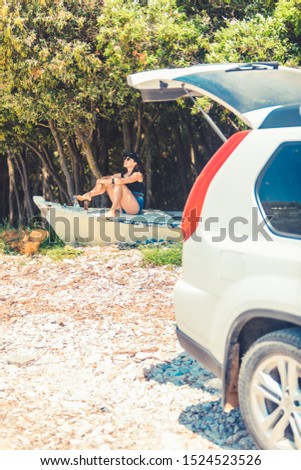 young woman sitting on boat at beach near car