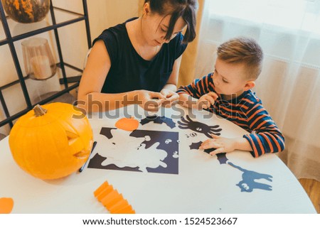 young mother with toddler son making craft spiders for halloween holiday