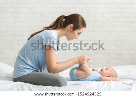 Strengthening exercises for babies. Young mother massaging her newborn baby in bed, side view