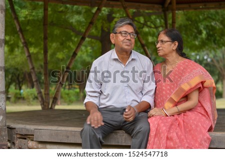 Senior citizen Indian couple smiling and laughing in the evening sitting closely in a park in summer in New Delhi, India. Concept love