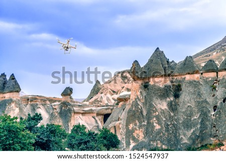 Quadcopter flies over the hill. White drone hovering in a bright blue sky. New technology in the aero photo shooting. Cappadocia, Central Anatolia Region of Turkey, Asia.