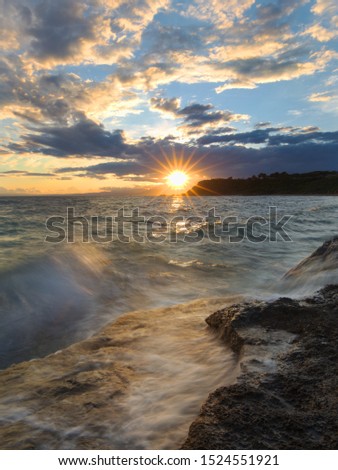 a stunning sunset with a lot of clouds and the sunburst over the sea with a wave coming and looking very smoothy
