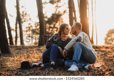 Beautiful romantic couple is having fun with their dog french bulldog on outdoors in the autumn forest at sunset