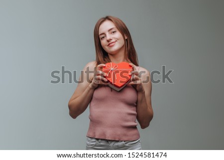 Girl holding a heart gift box on grey background