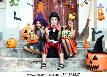 Two young girls and boy in costumes sitting on porch with halloween decorations