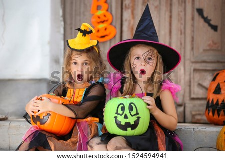 Young girls in halloween costumes sitting on porch with pumpkin buckets