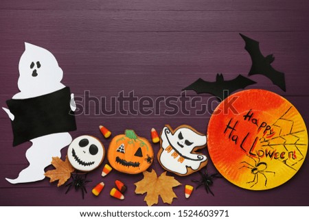 Paper ghost with candies, gingerbread cookies and text Happy Halloween on wooden background