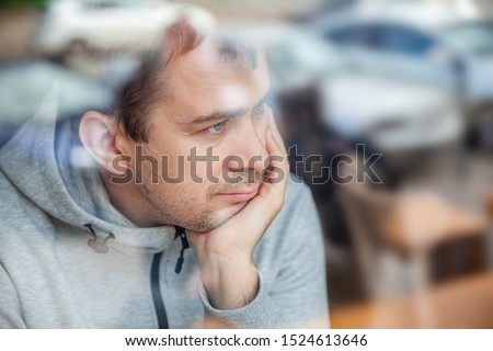 Sad pensive handsome man leaning head on hand in cafe, looking through a window with reflections. Royalty-Free Stock Photo #1524613646