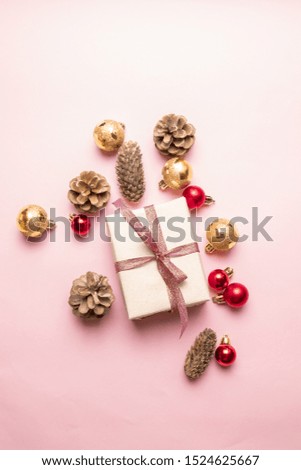 Creative Christmas or New Year composition of gift box with red ribbon, pine cone, gold and red balls on a pink background. Vertical layout