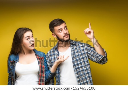 Young, happy couple in basic clothing smiling while putting up fingers isolated over yellow background. Place for some text.