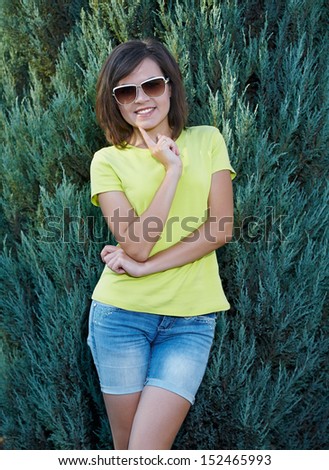 Attractive young woman in a yellow shirt and glasses. Woman in a beautiful park. Holding her finger on her chin.