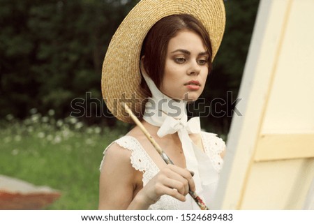 young woman outdoors an easel in a hat paints a picture