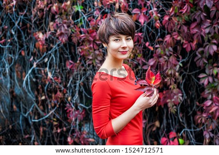 Autumn romantic Beauty. Portrait of Cute Woman in red dress with Fall Leaves in the Park Outdoors in Sunny Day. Seasonal dreamy mood. Fresh skin and healthy smile. Copy space