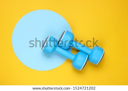 Plastic dumbbell on yellow background with blue pastel circle. Top view. Minimalistic sport concept. Top view