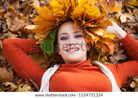 Close up portrait of a young beautiful woman with a wreath of maple leaves posing in autumn park