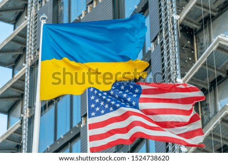 American and Ukrainian flags fly against the blue sky and part of the building. Patriotism.