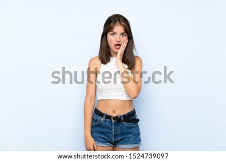 Young woman over isolated blue background surprised and shocked while looking right