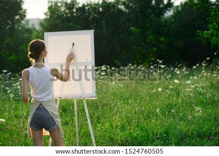young beautiful woman draws on a white canvas on the nature
