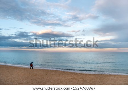 photographer with umbrella in the rain, at the sea shore, walks and takes pictures of the sea, with wonderful sky and clouds at the background, at the sunset