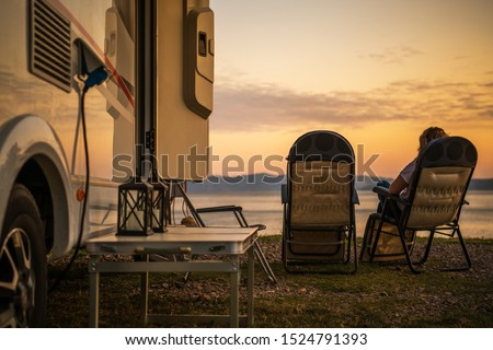 Scenic RV Campsite Pitch. Camper Van In the Recreational Vehicles Park. Woman Relaxing on a Chair and Watching Sunset Over the Sea.
 Royalty-Free Stock Photo #1524791393