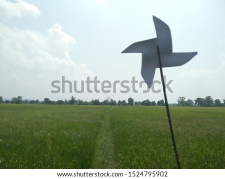 Paper wind turbine in grass field with blue sky