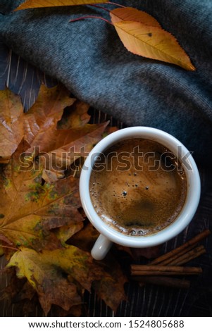 Orange autumn leaves and hot coffee on wooden table.