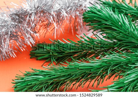 Background in the form of Christmas tree decorations - a green branch of artificial spruce and silver rain on a coral background, side view from above, close-up
