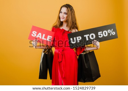 young woman in red dress with sale up to 50% sign and paper shopping bags isolated over yellow